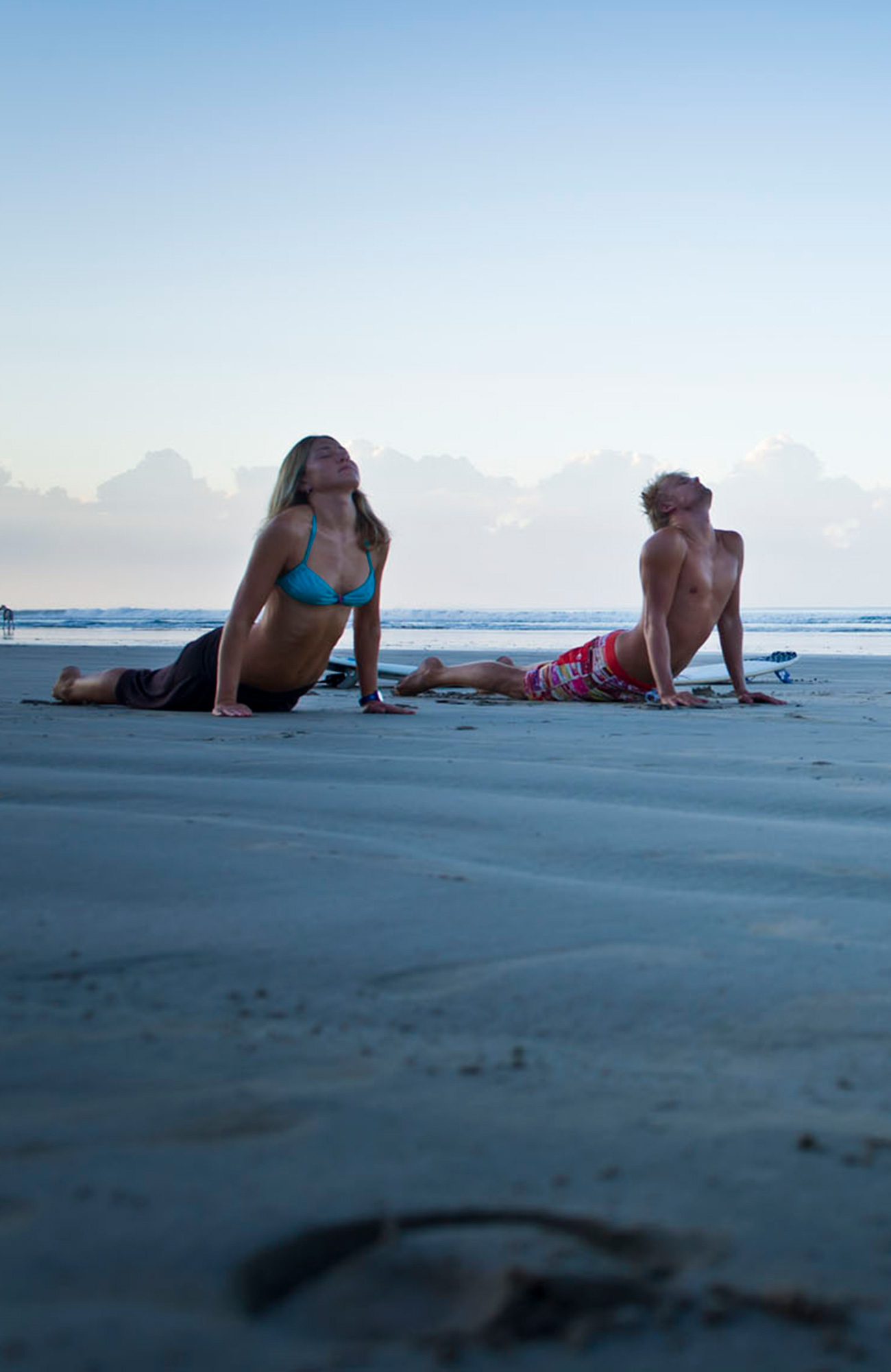 Image of two people holding the cobra pose and practising yoga on a beach - KILROY
