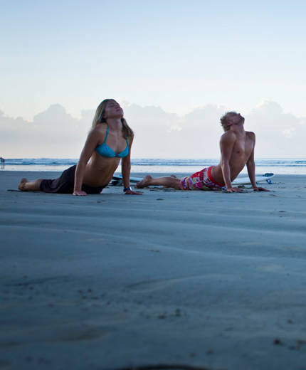 Image of two people holding the cobra pose and practising yoga on a beach - KILROY
