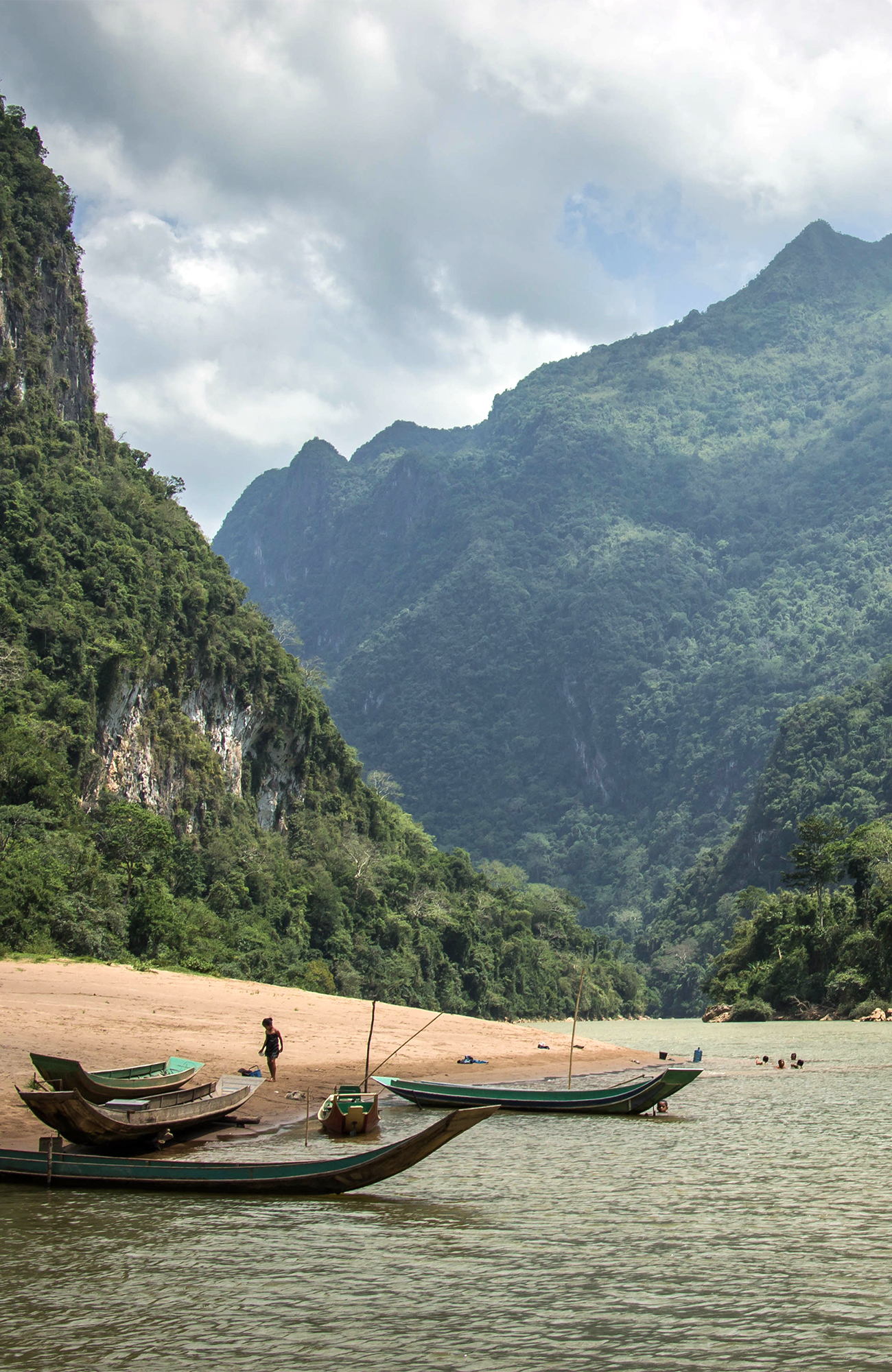 Image of a karst river landscape in Laos with boats and people playing in the water - KILROY