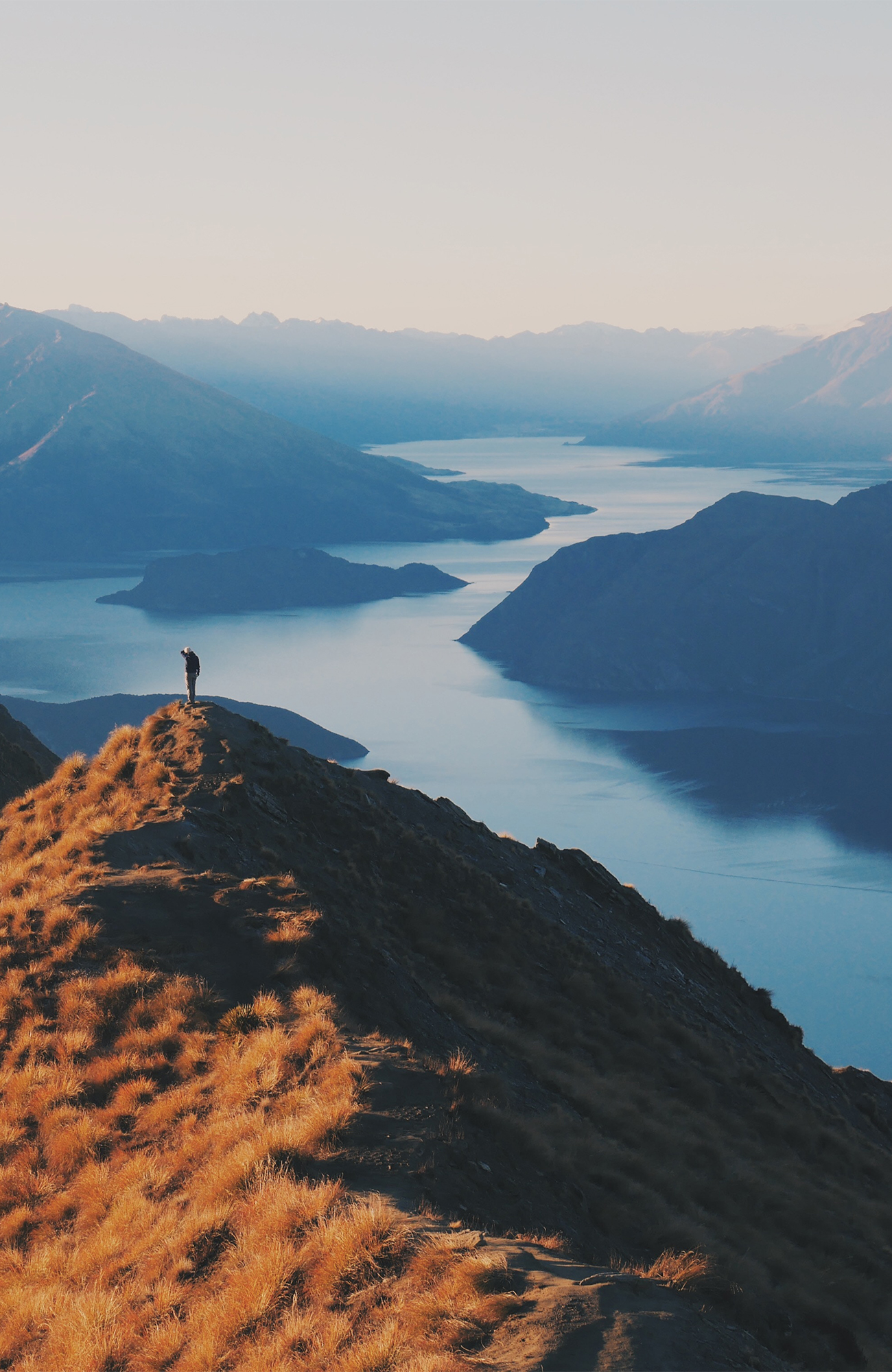 Image of a hiker at the top of a hill overlooking a beautiful lake in New Zealand - KILROY
