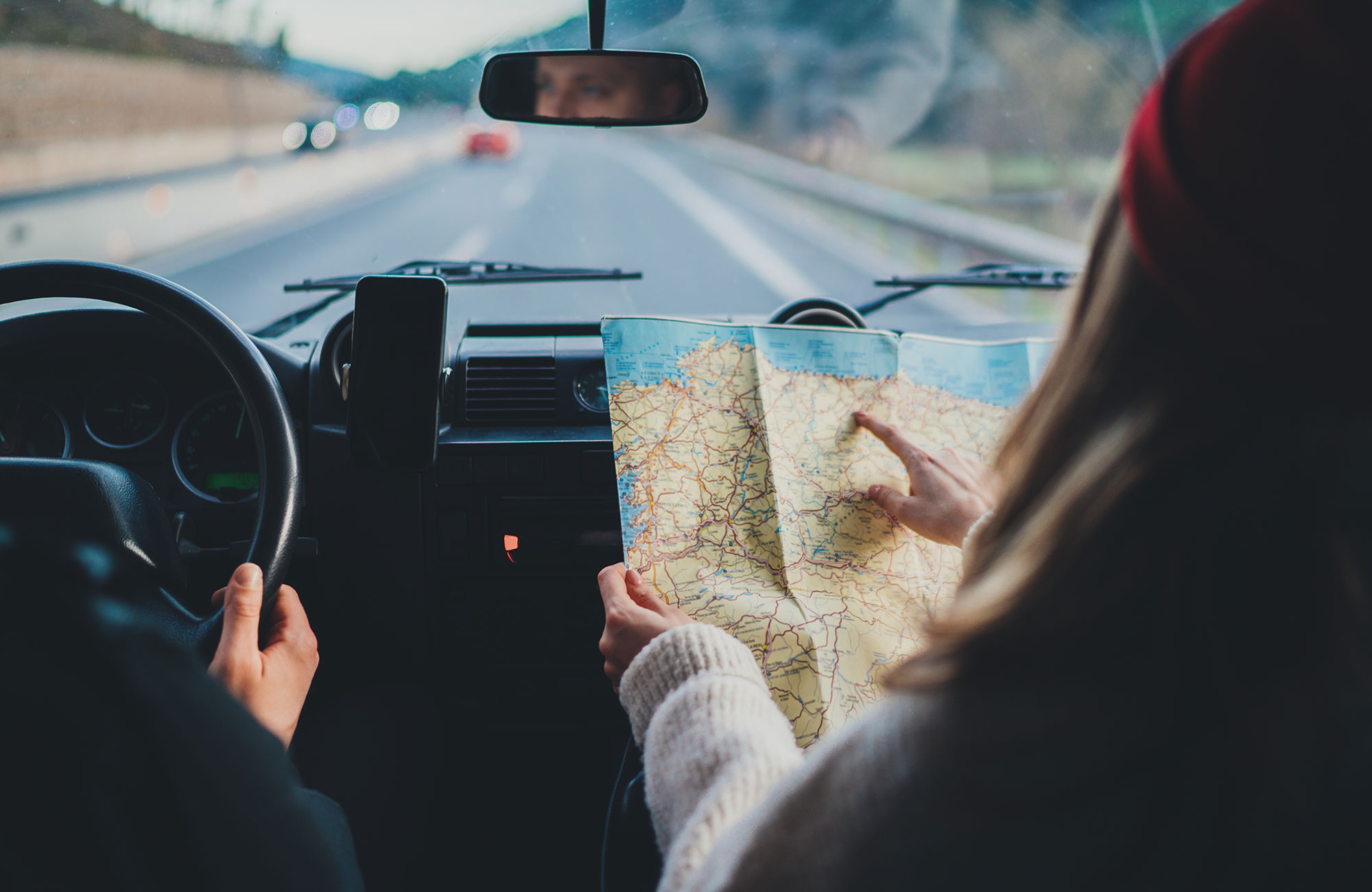 Image of a couple driving a car while the passenger points at a map - KILROY