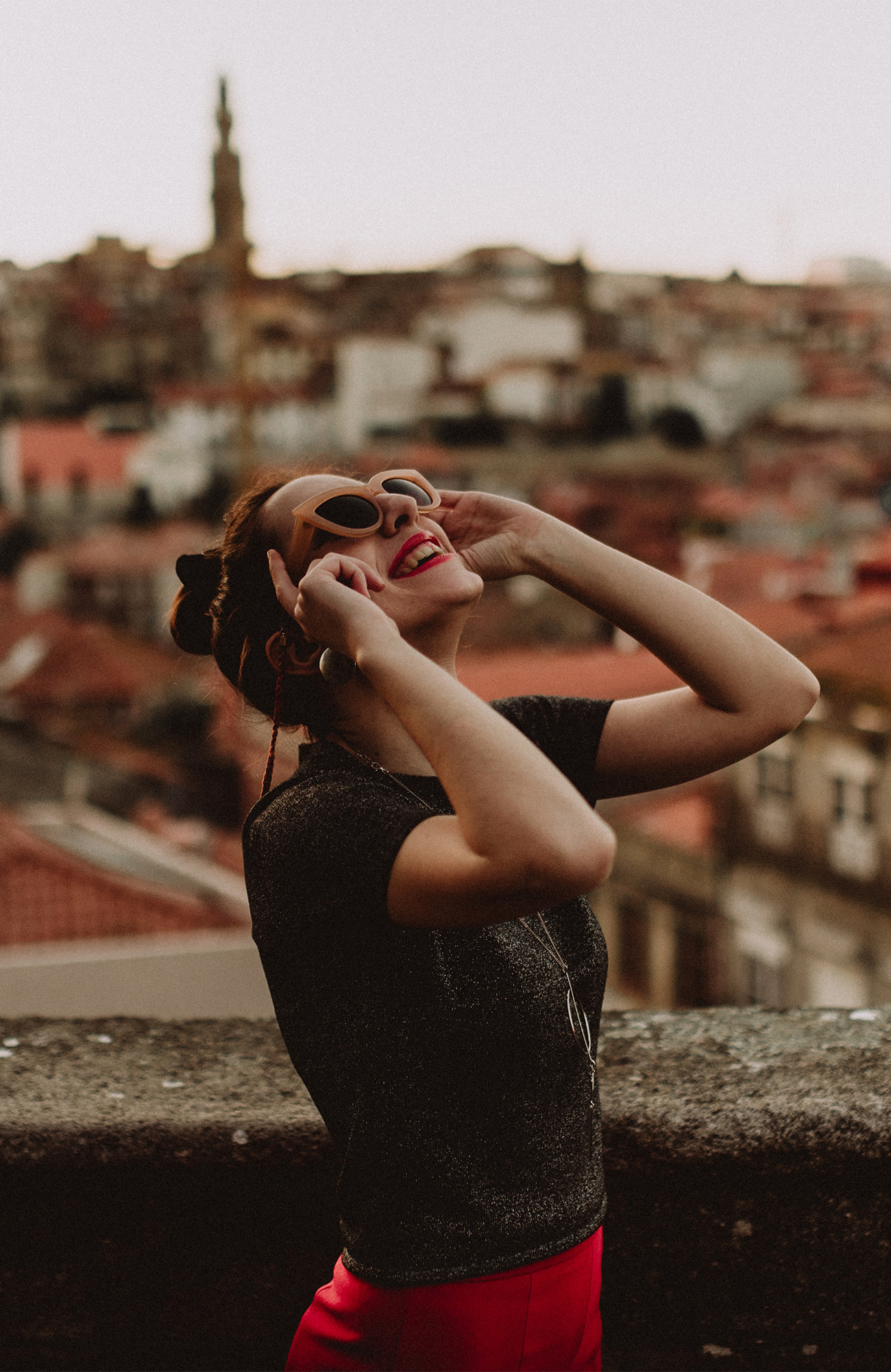 Image of a woman wearing sunglasses and looking up to the sky in a city in Europe - KILROY