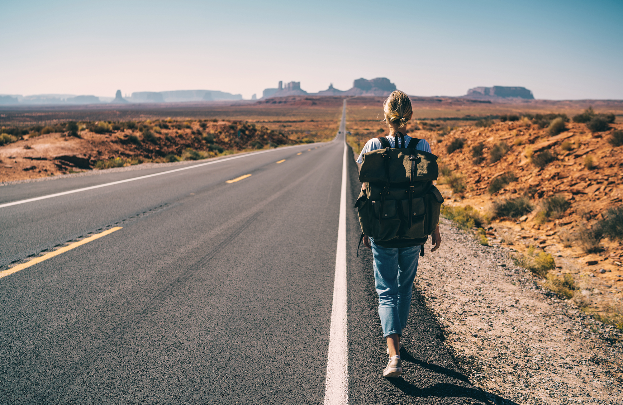 Image of a woman with a backpack walking along a highway in the USA - KILROY