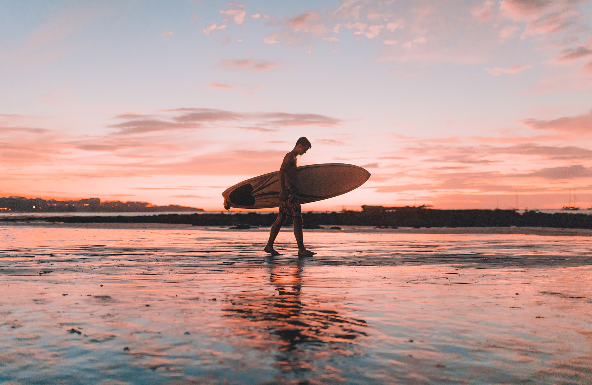 Image of a man walking with a surfboard against a beautiful sunset - KILROY