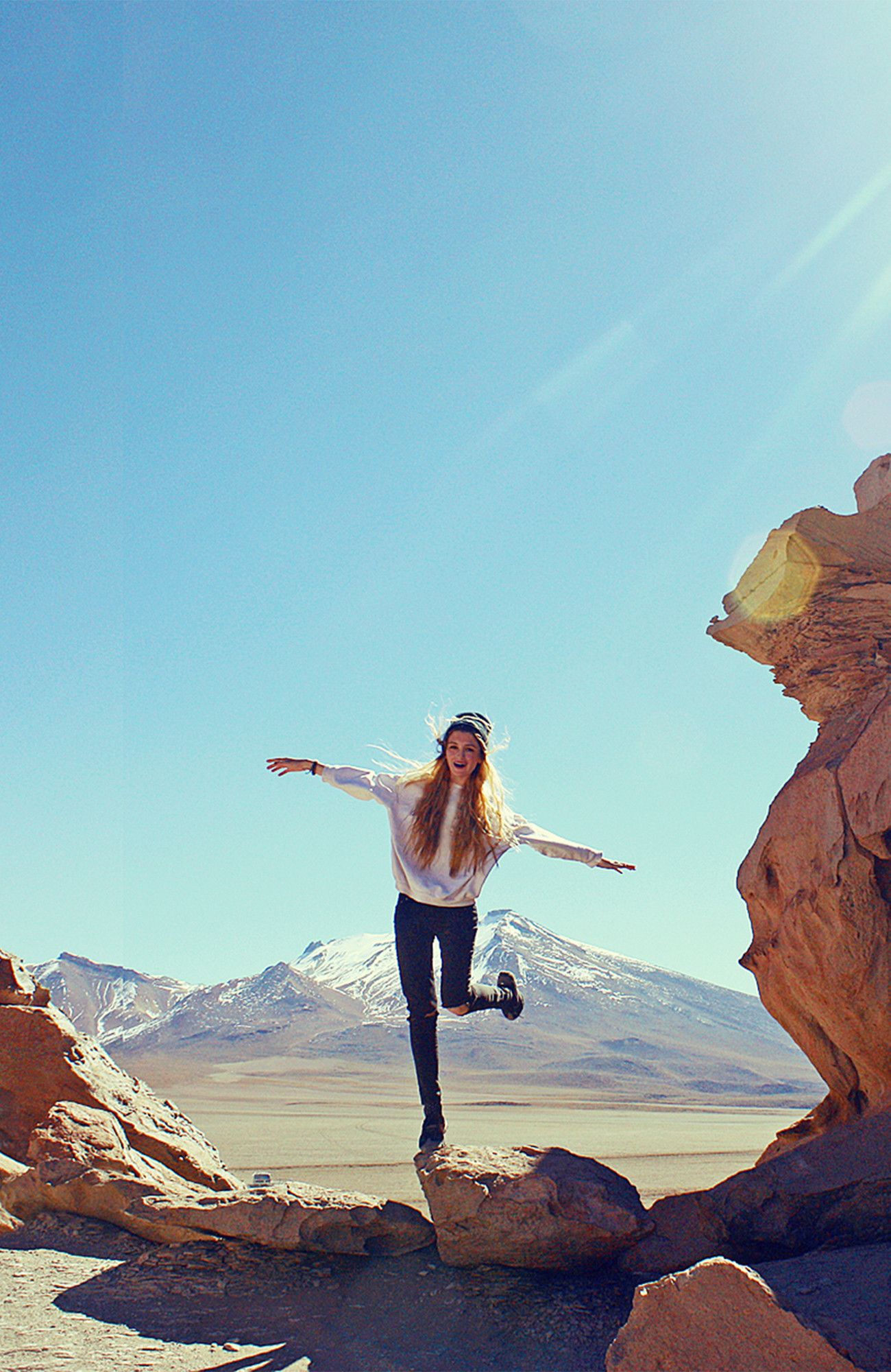 Image of a female traveller posing on a rock in a mountainous landscape in Bolivia - KILROY