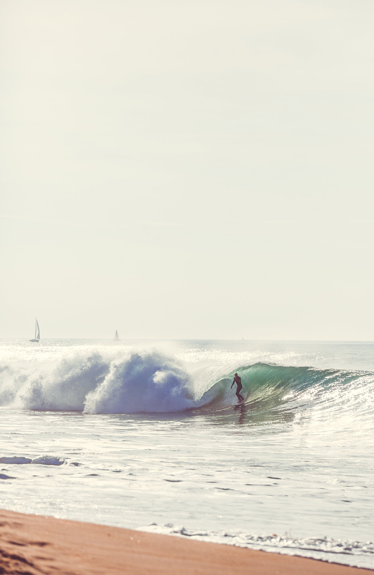 Image of a surfer catching a wave with sailboats in the distance - KILROY
