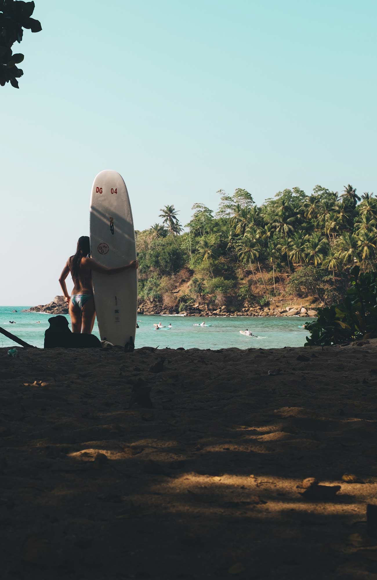 Image of a female surfer holding a board and looking out at a bay in Sri Lanka - KILROY