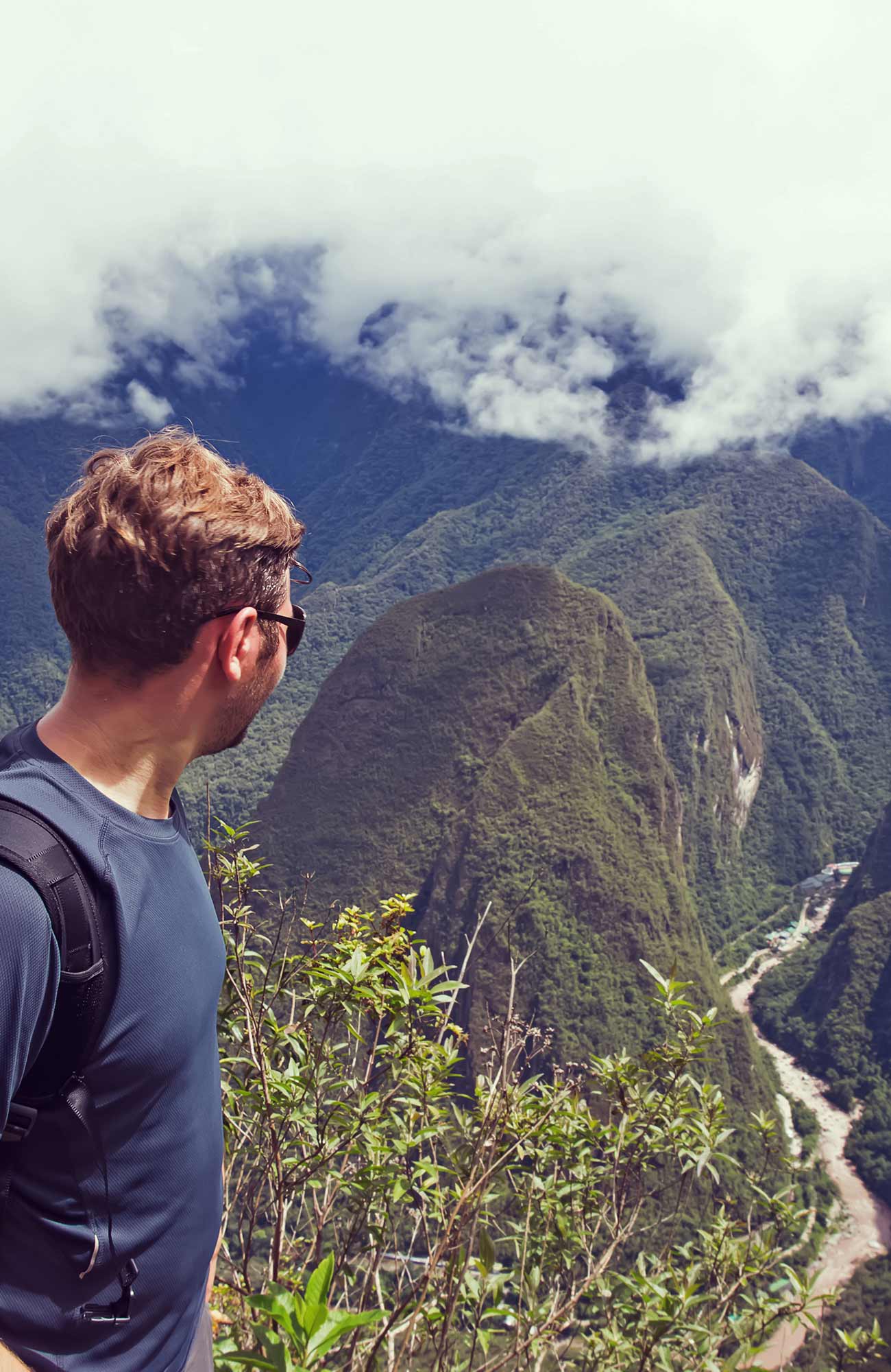 Image of a traveller looking out over a river between towering mountains in Peru - KILROY