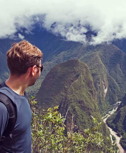 Image of a traveller looking out over a river between towering mountains in Peru - KILROY