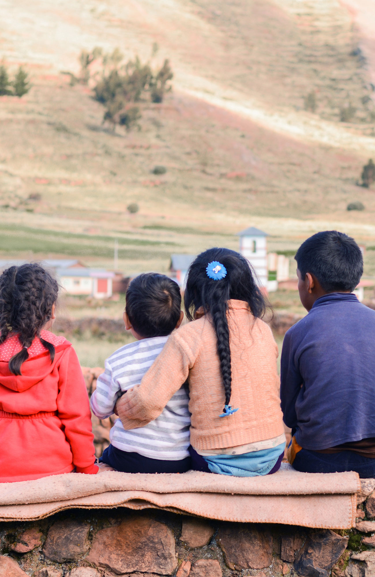 Image of young children sitting on a stone wall in a village in Ecuador - KILROY