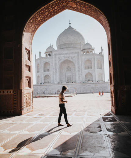 Image of a traveller walking near a doorway looking out towards the Taj Mahal in India - KILROY