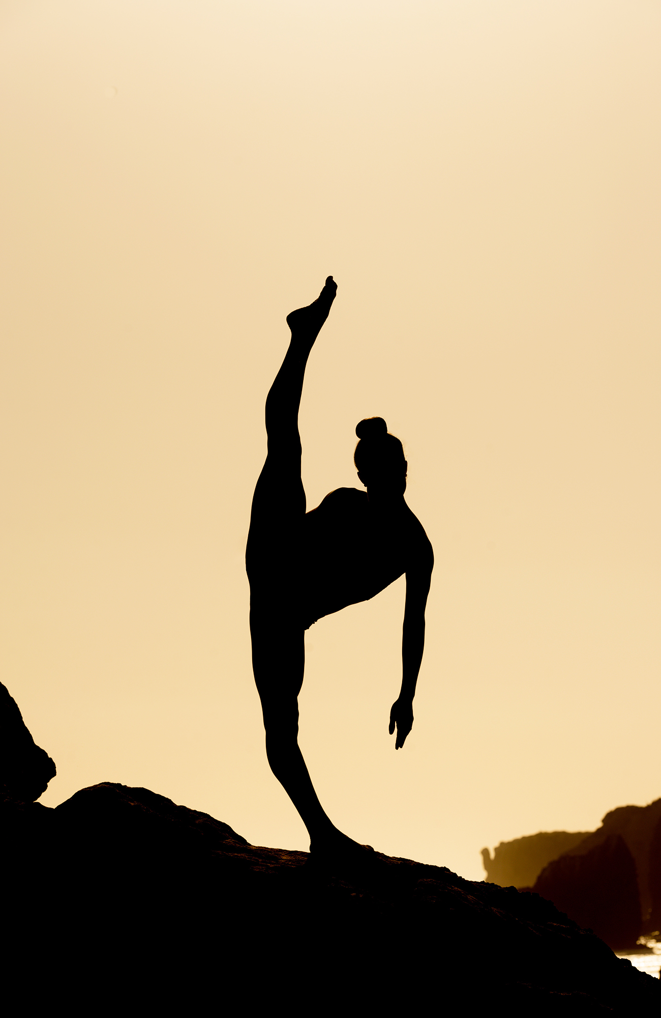 Image of the silhouette of a woman holding a yoga pose on a rock near a beach at sunset - KILROY