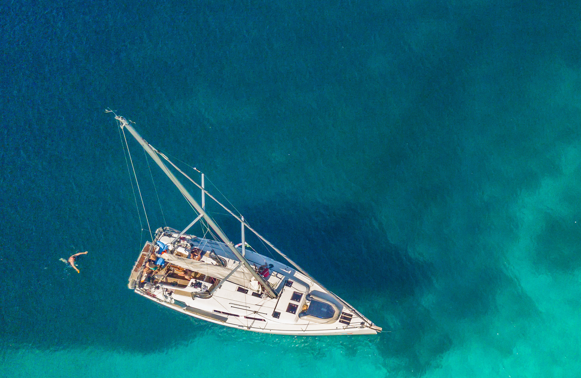 Aerial image of a sail boat anchored on crystal clear waters - KILROY