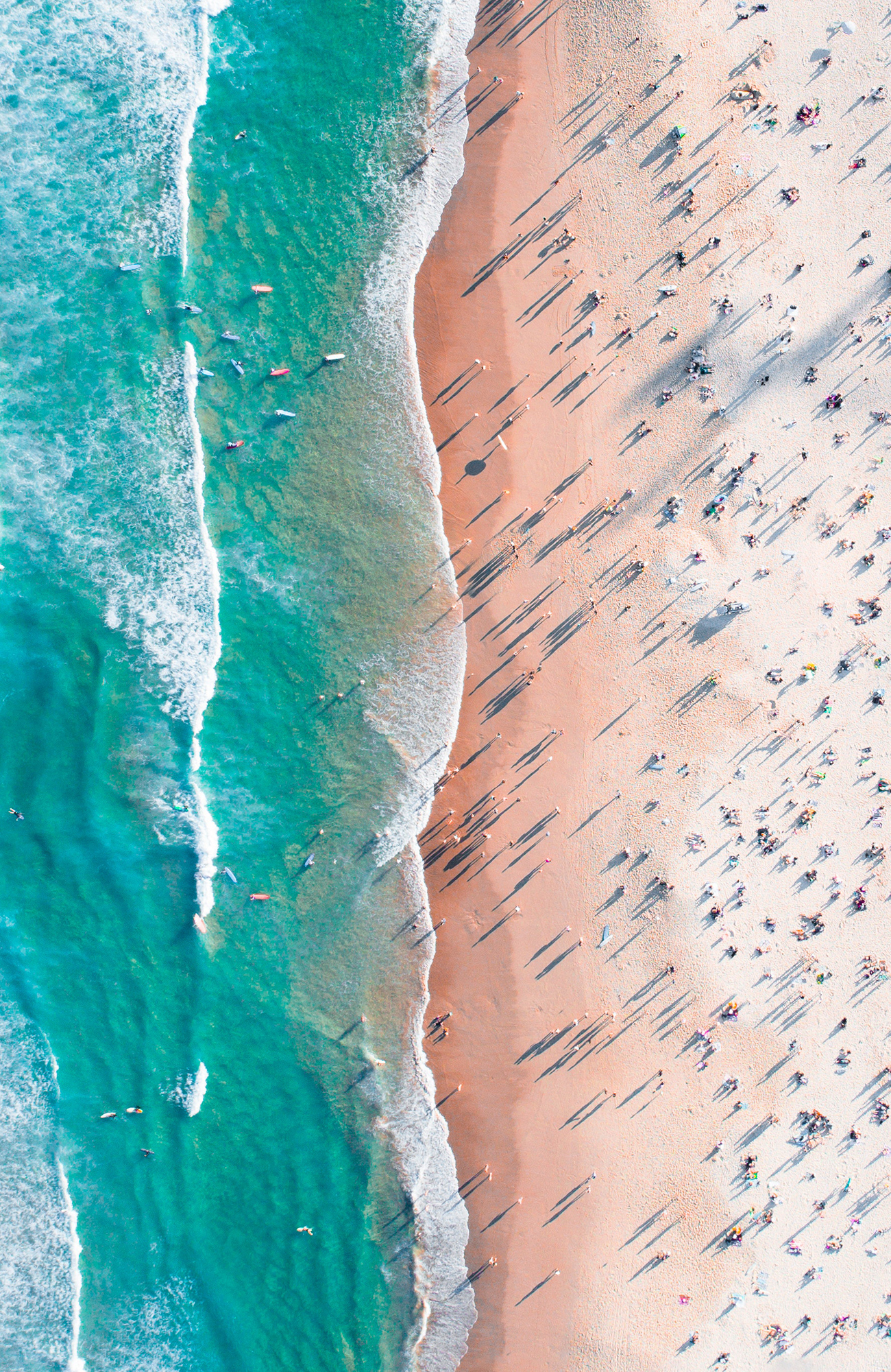 Aerial view of a beach in Australia with surfers on the water and sunbathers on the sand - KILROY