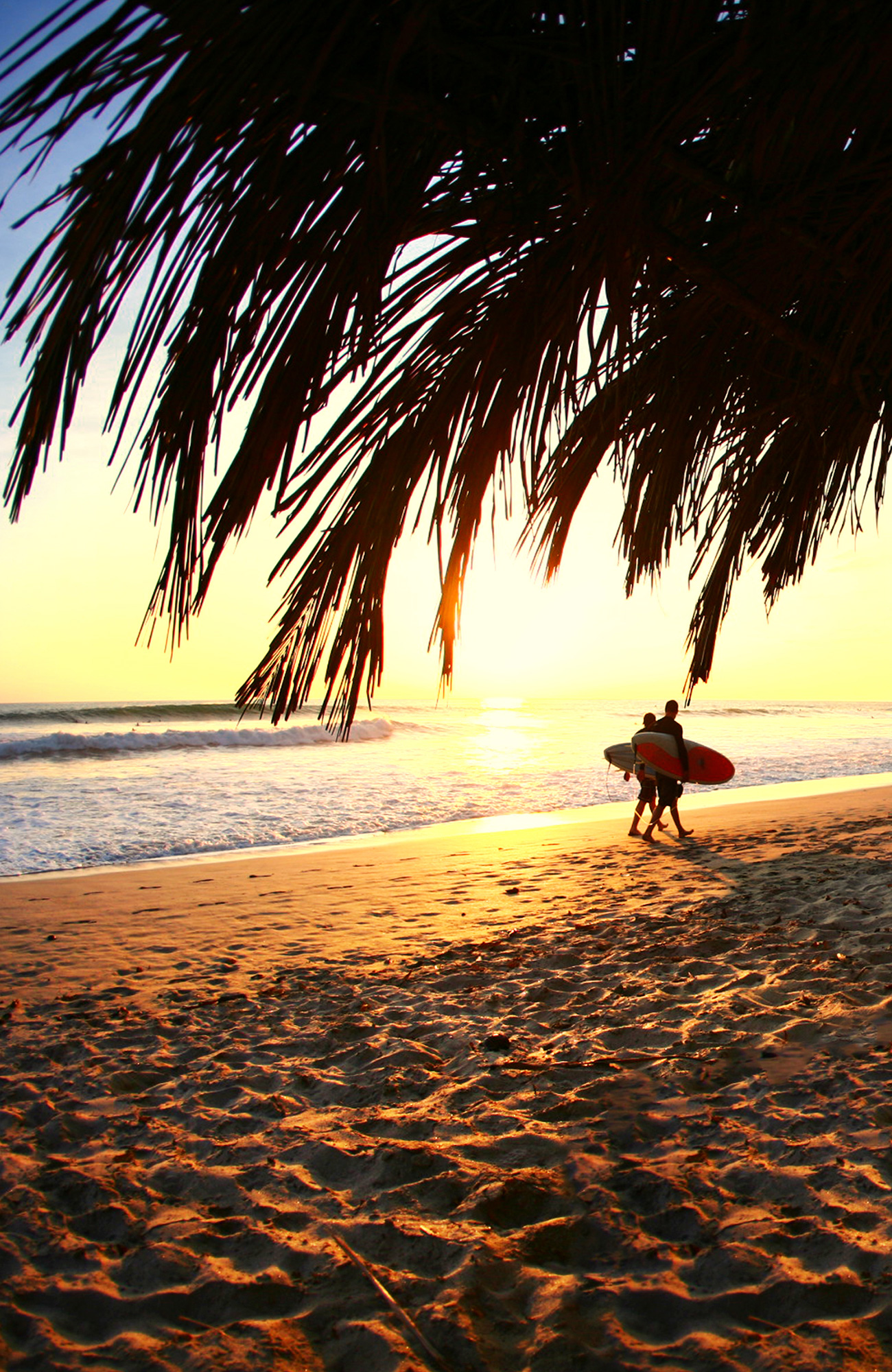 Image of two surfers walking along a beach at sunset in Costa Rica - KILROY