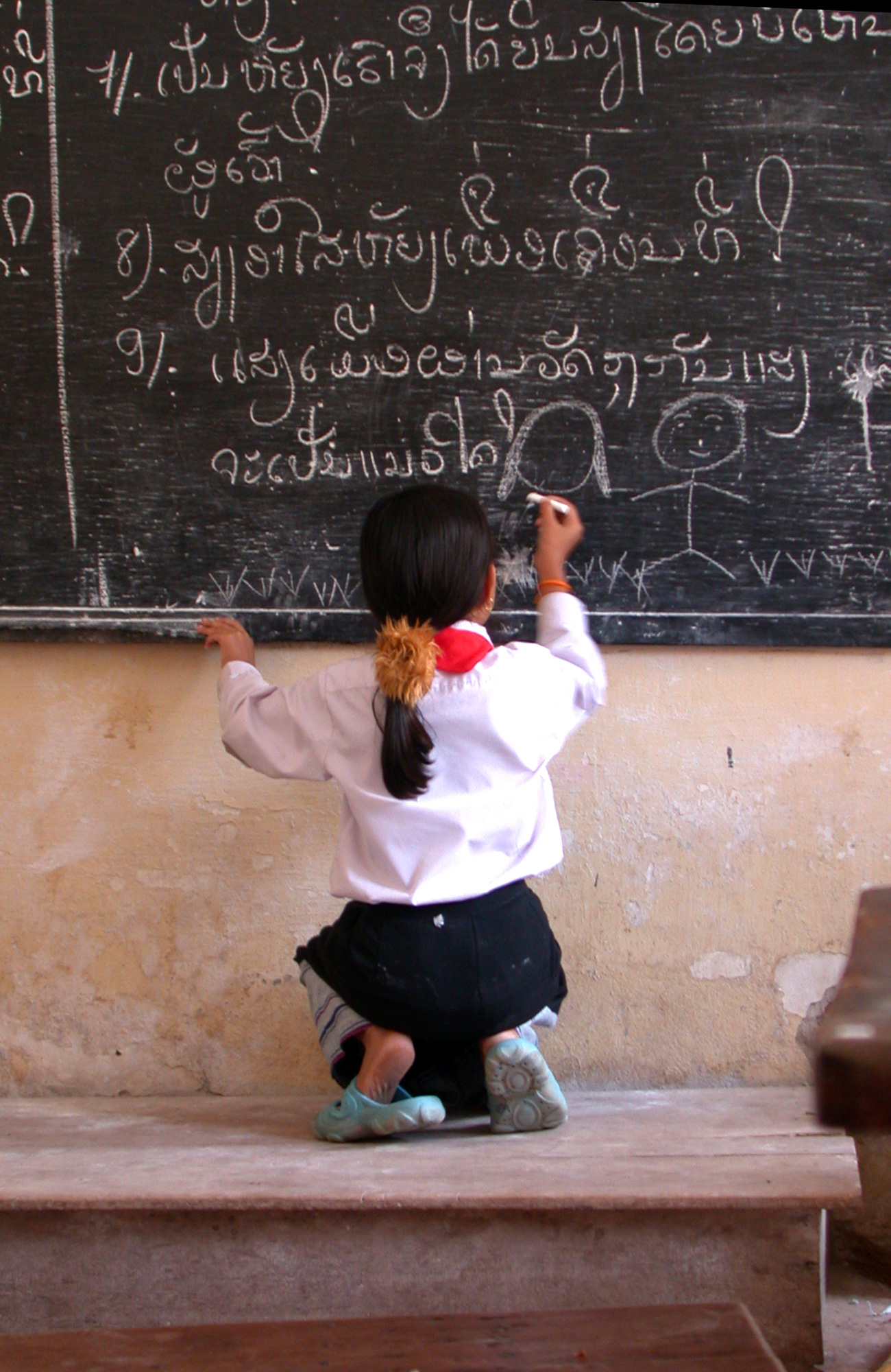 Image of a young Thai girl writing on a chalkboard in a school - KILROY