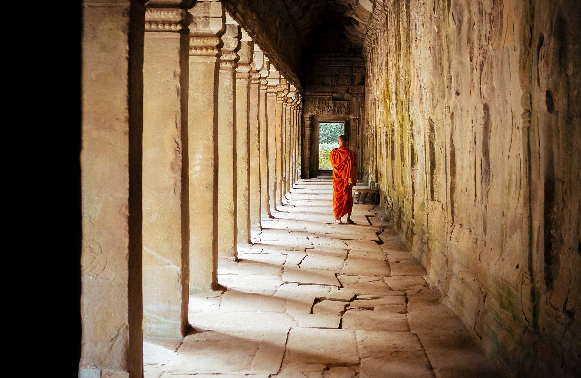 Image of a young monk walking along an ancient corridor at Angkor Wat in Cambodia - KILROY