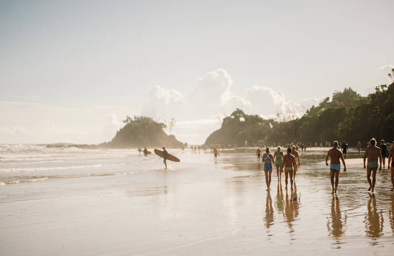 Surfers en wandelaars tijdens zonsondergang bij Byron Bay, Australië