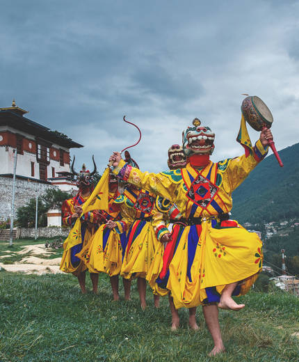 Image of masked dancers in colourful robes performing at a festival in Bhutan - KILROY