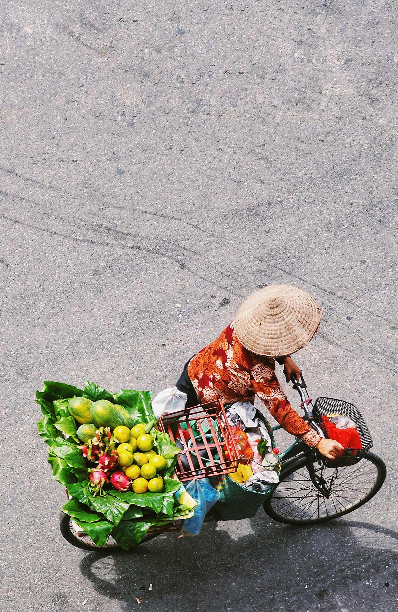 Image of a Vietnamese woman pushing a bike topped with baskets of fruit and vegetables - KILROY