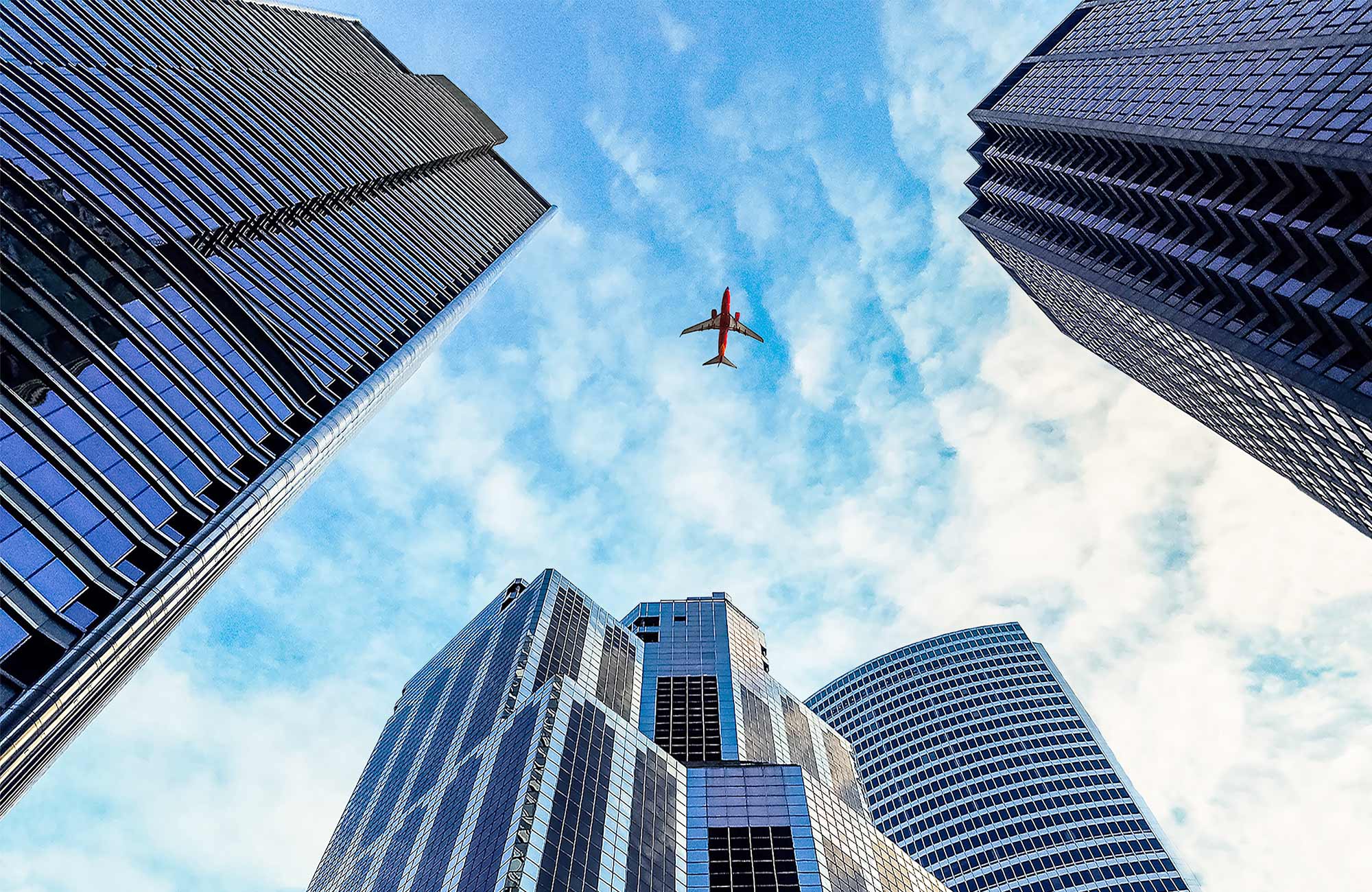 Image looking up at a plane flying over skyscrapers - KILROY