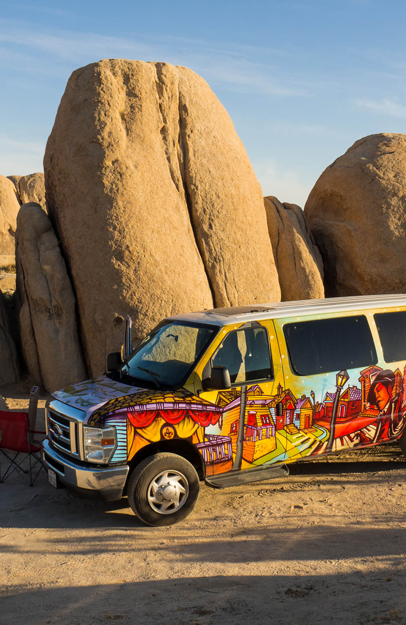 Image of a colourful campervan parked next to a tall boulder in the desert - KILROY