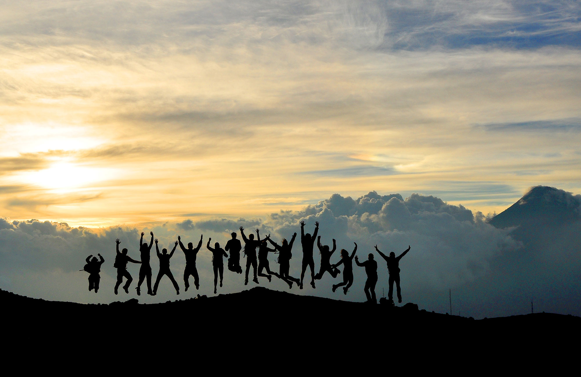Image of a group of travellers jumping in silhouette on a mountain ridge - KILROY