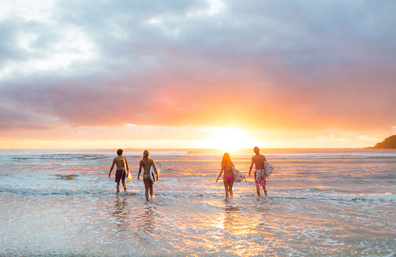 Image of a group of surfers on the beach at sunset - KILROY