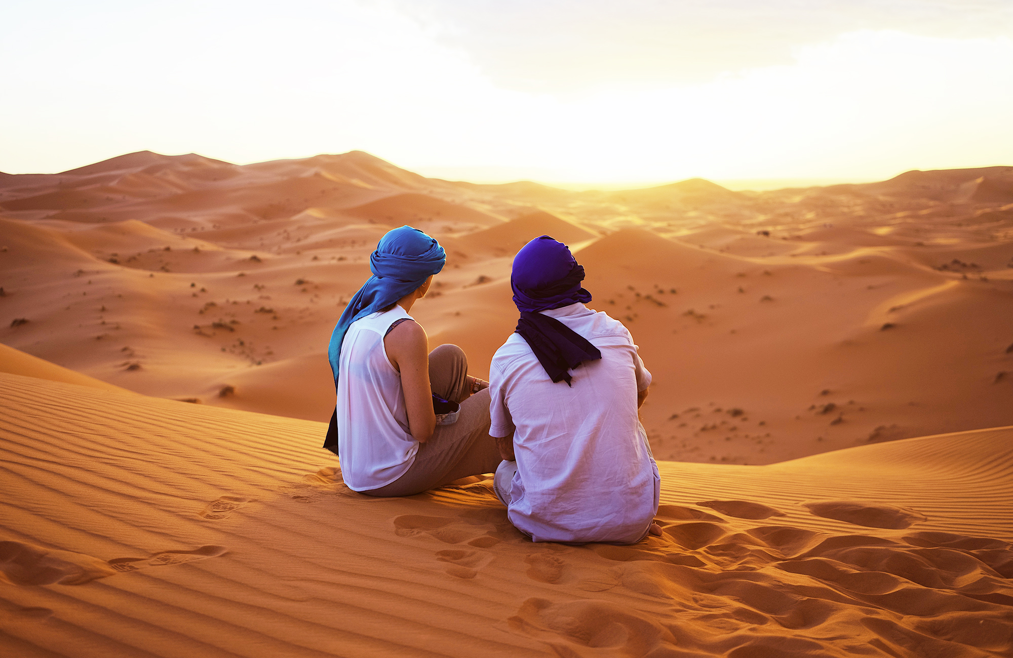 Image of a couple sitting on the Saharan sand dunes in Morocco - KILROY