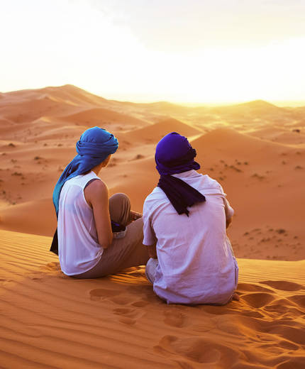 Image of a couple sitting on the Saharan sand dunes in Morocco - KILROY