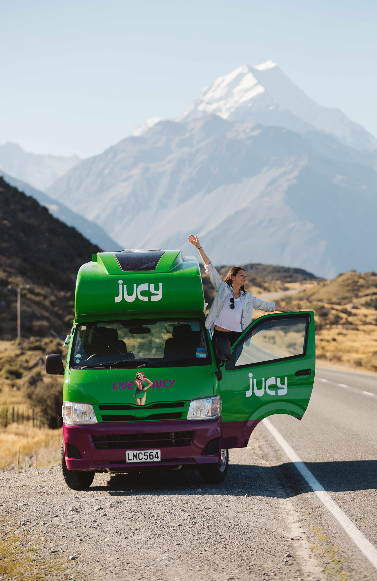 Image of a woman hanging out of a Jucy Condo campervan in New Zealand - KILROY