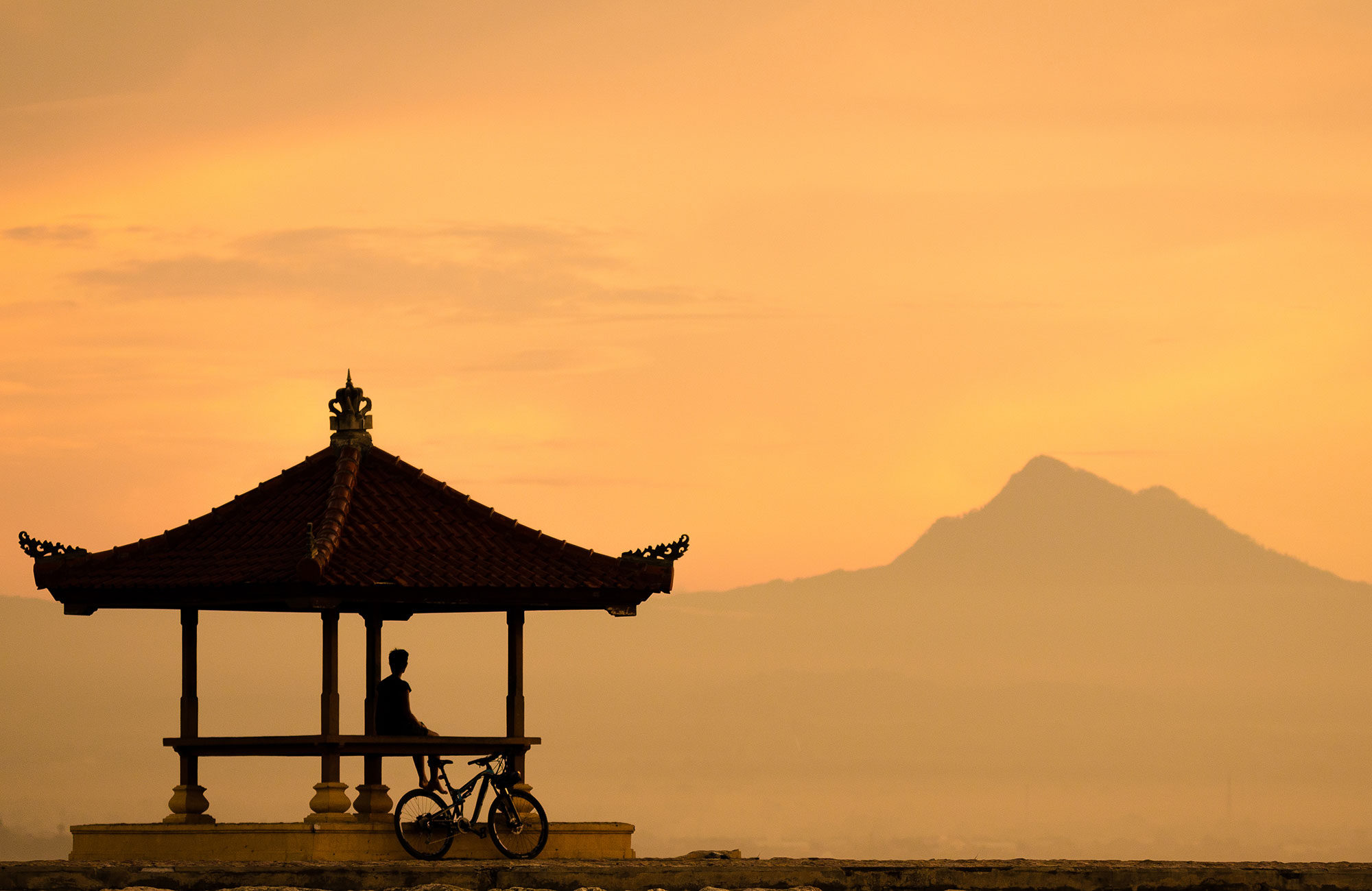 Jongen met de fiets geniet van de zonsondergang boven Karang Beach in Sanur, Indonesië