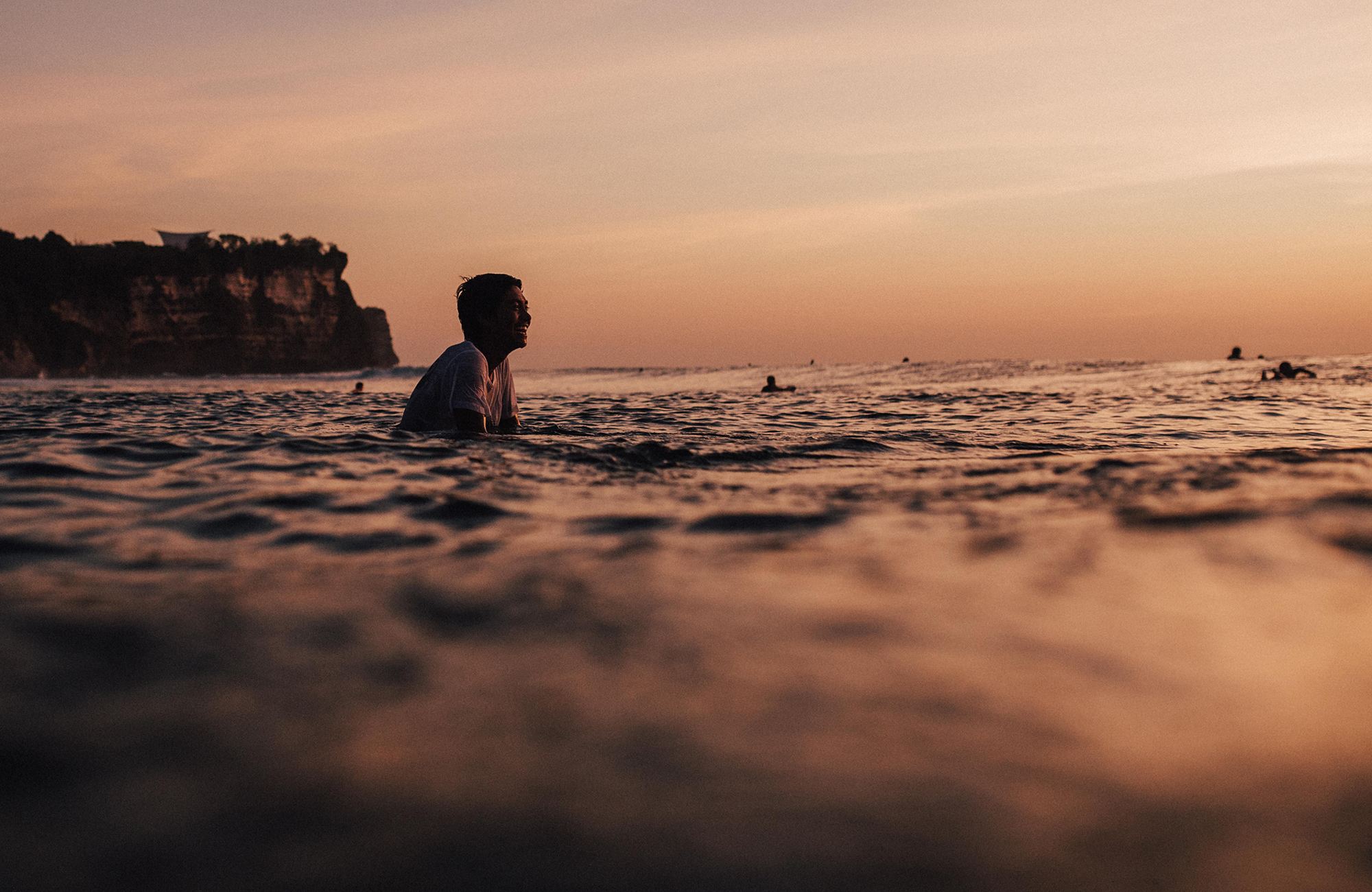 A surfer in the water in Bali at dusk - KILROY