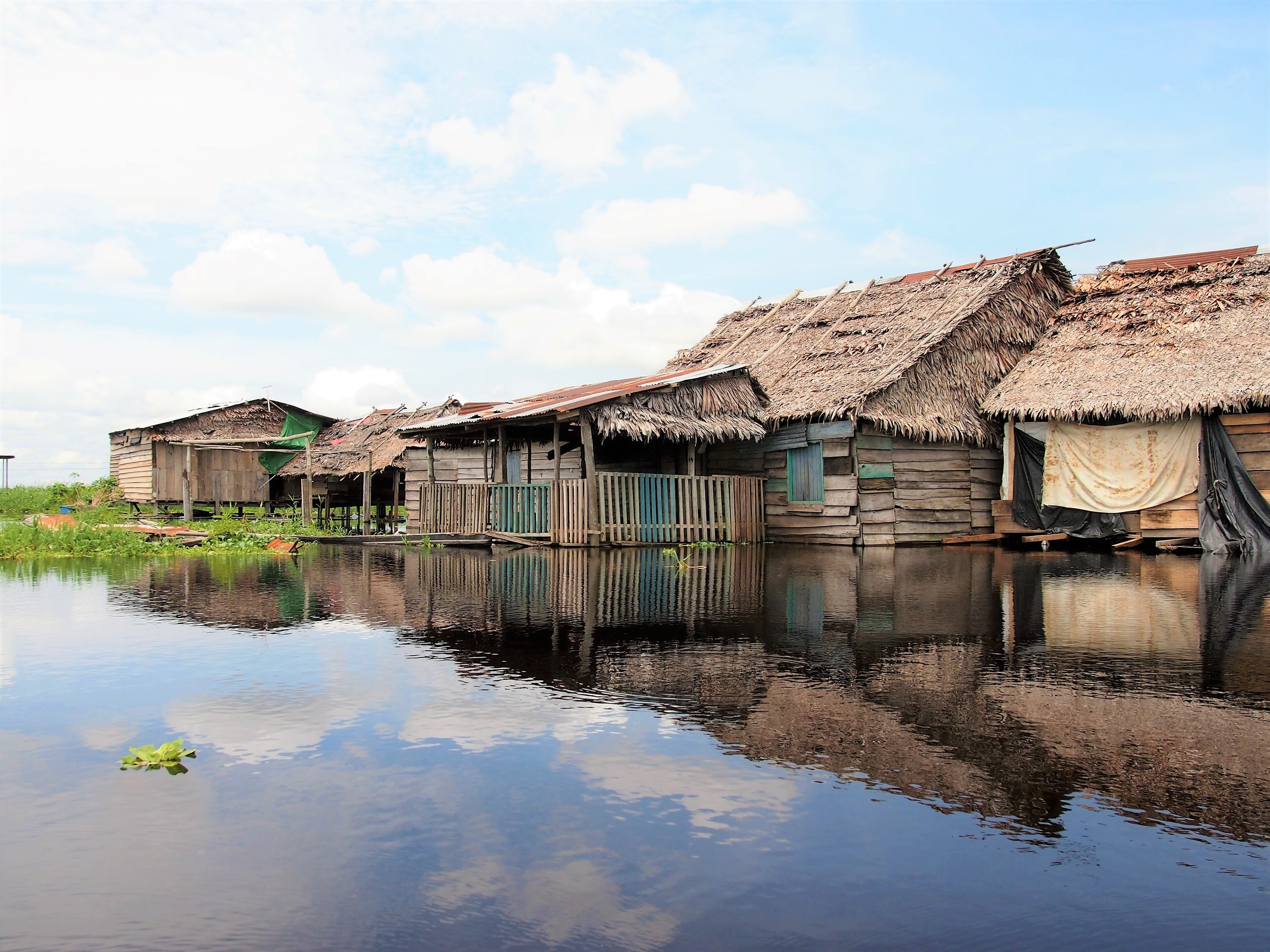 Image of traditional wooden huts along a river in the Peruvian Amazon - KILROY