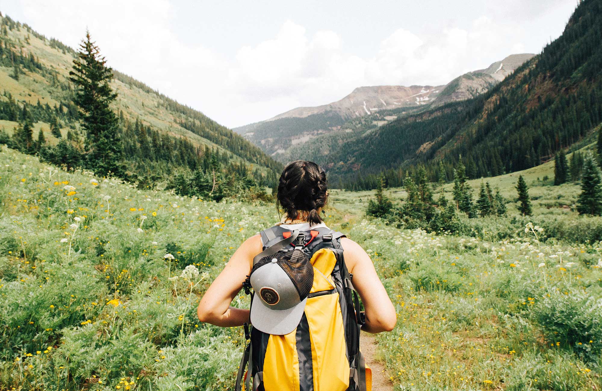 A girl with a yellow backpack trekking in beautiful landscape - KILROY UK
