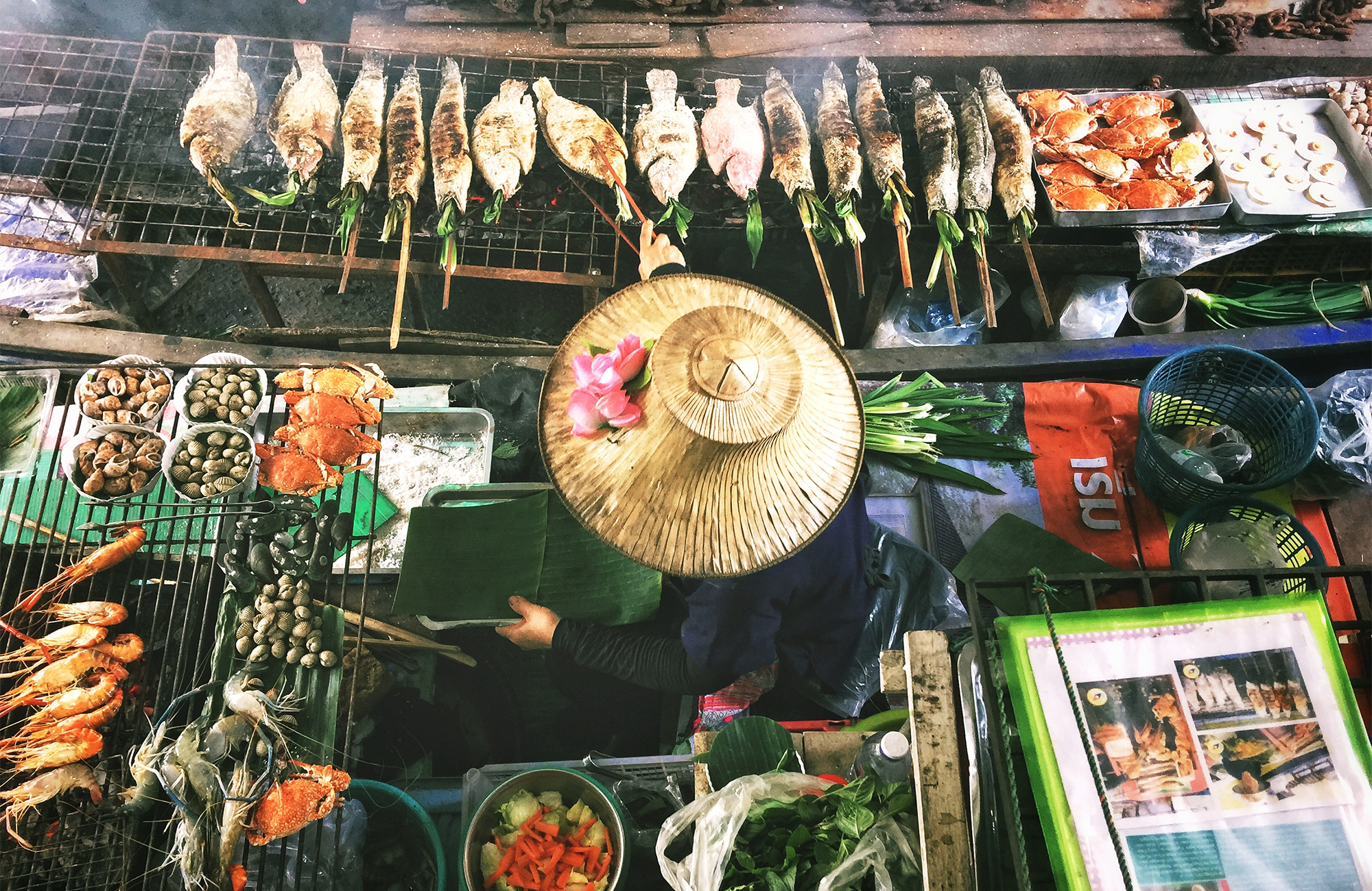 Image of a woman wearing a conical hat and serving up delicious fried fish at a food stall in Thailand - KILROY