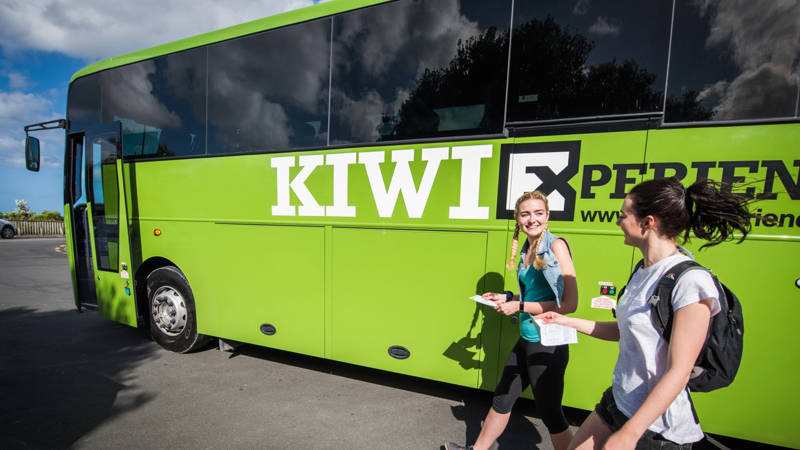 Image of two young travellers beside a green Kiwi Experience bus in New Zealand - KILROY