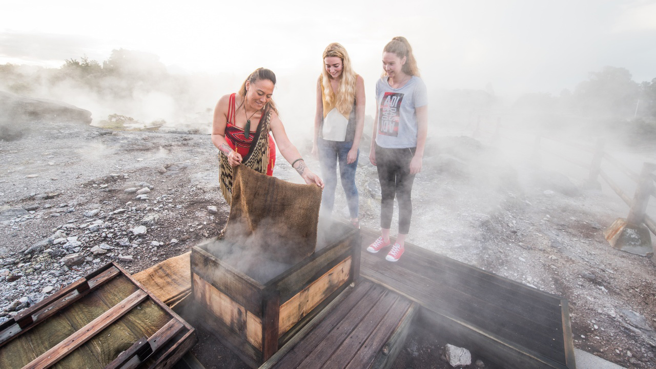 Image of two young female travellers at a traditional Maori hangi in New Zealand - KILROY