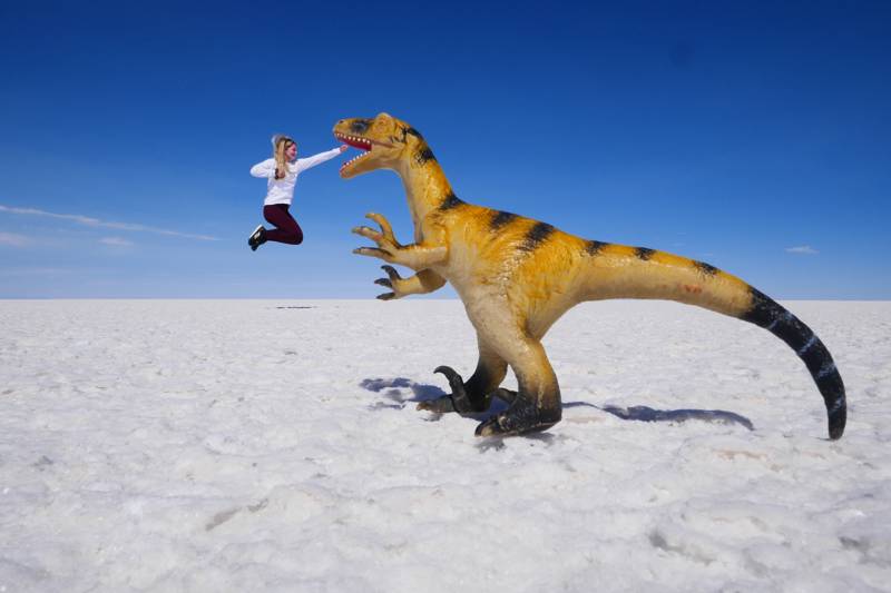 Image of a traveller posing with a dinosaur toy on the salt flats of Bolivia - KILROY
