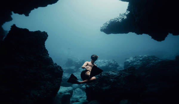 Freediver In The Ocean With A Lot Of Big Rocks Surrounding Him