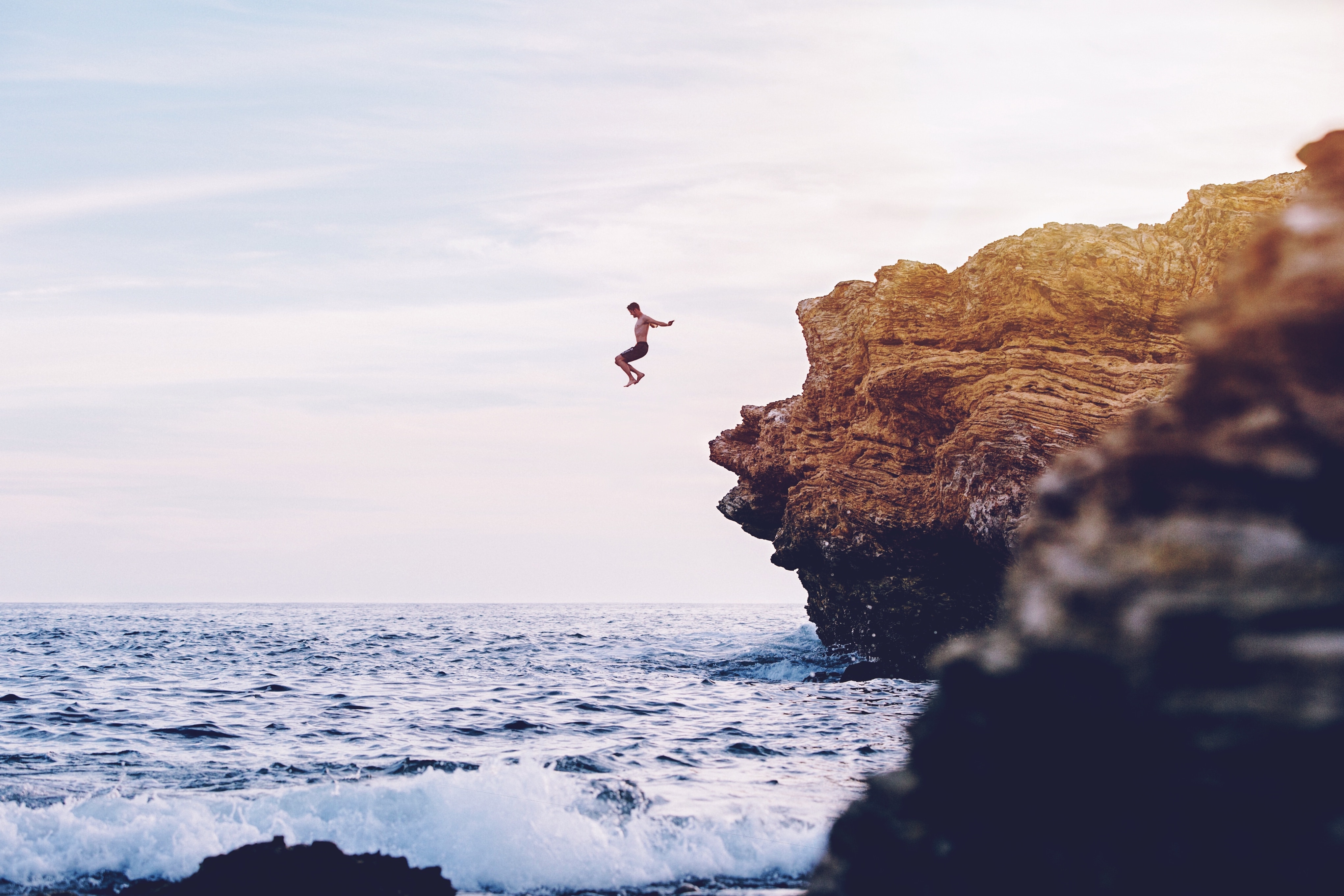 Image of a young man jumping from a cliff into the sea