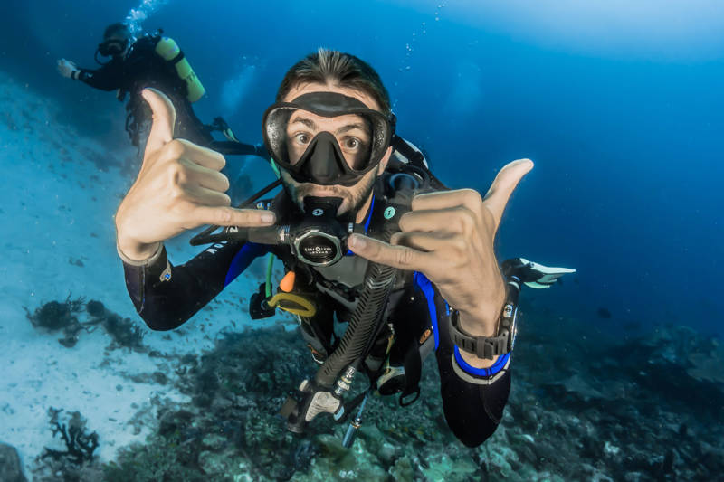 Two guys diving in the Maldives with one guy making a sign with his hands