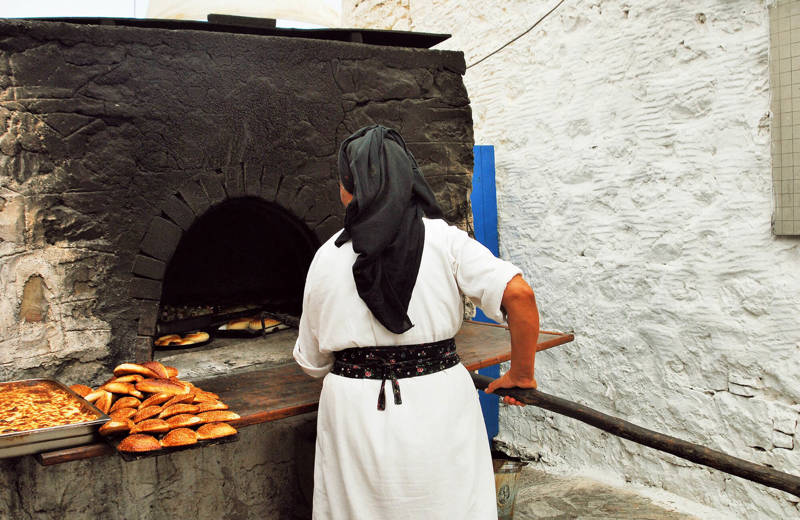 Image of a Greek woman preparing bread in a traditional oven - KILROY