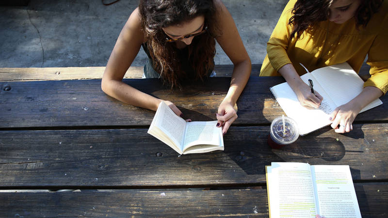 Image of a group of travellers reading books on a bench - KILROY