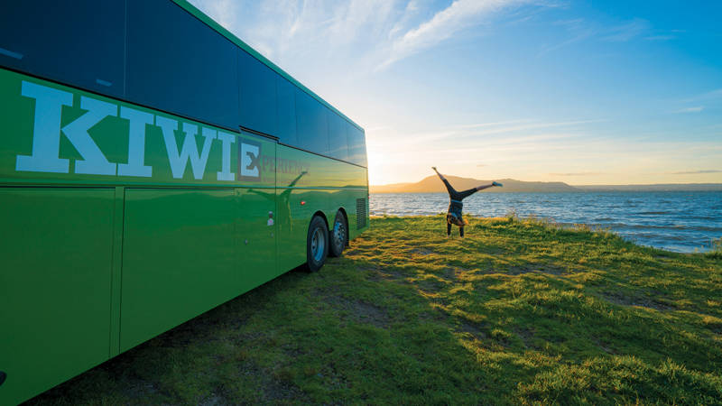 Image of a woman doing a cartwheel next to a Kiwi Experience bus - KILROY