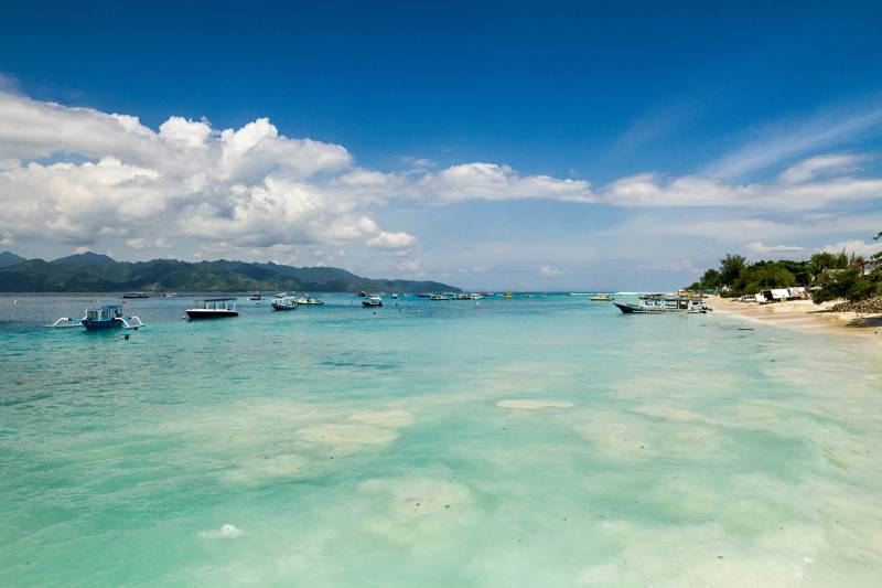 Turquoise waters and traditional fishing boats off a sandy beach on Gili Trawangan island in Indonesia - KILROY