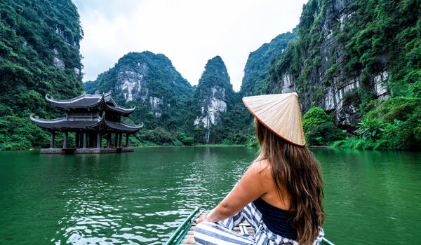 Toerist met traditionele hoed voor een meer tussen de bergen van Ninh Binh in Vietnam