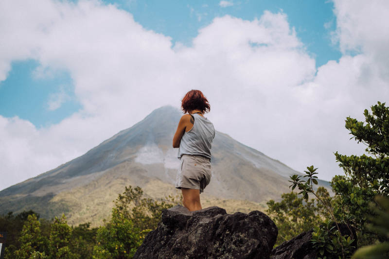 Image of a woman standing on a rock in front of Arenal Volcano in Costa Rica - KILROY